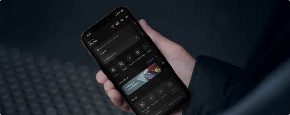 Mão segura um celular com o app do C6 Bank, destacando a Conta Global no menu de serviços.