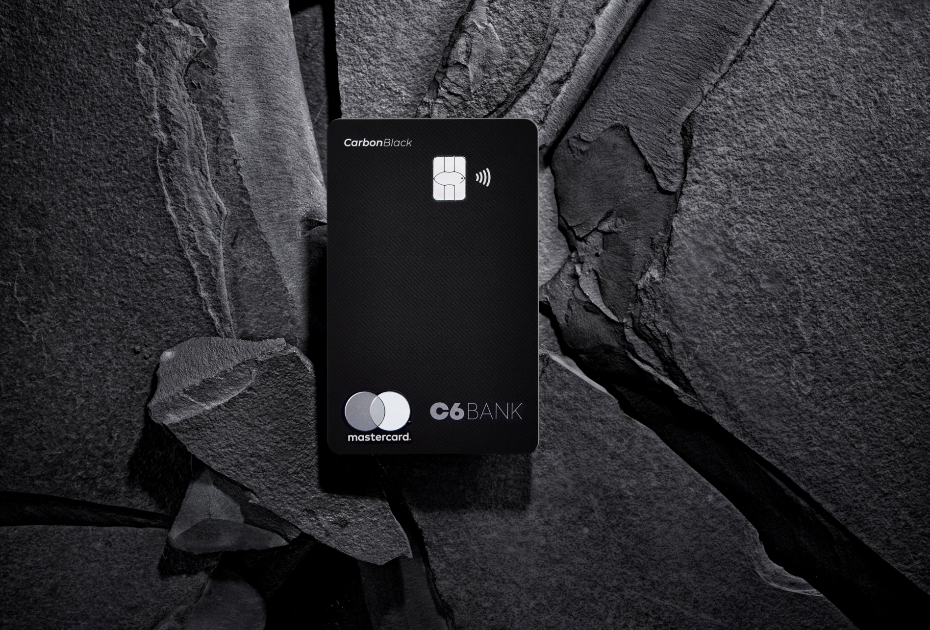 Cartão C6 Carbon Mastercard Black sobre pedra escura, destacando sua textura sofisticada.