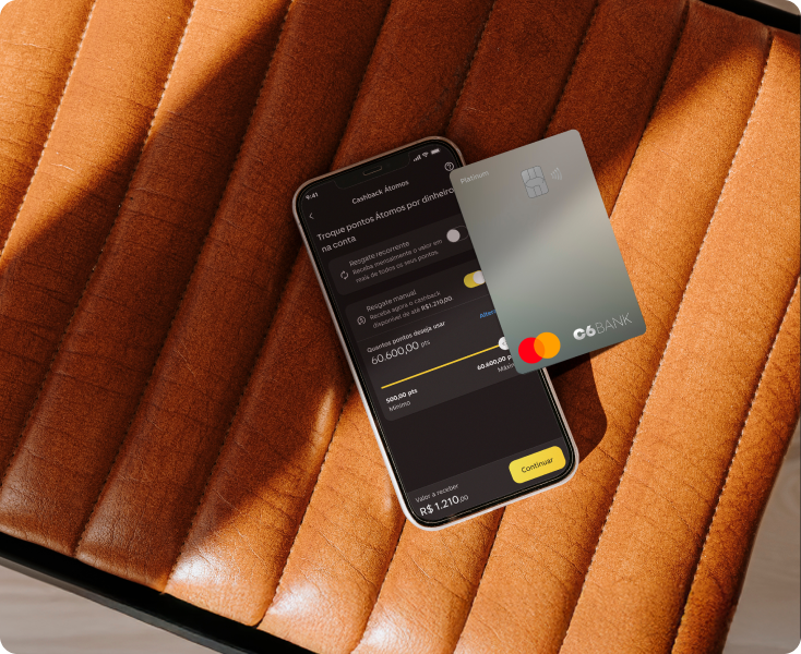 Cartão C6 Platinum e celular com app do banco, sobre assento de couro.