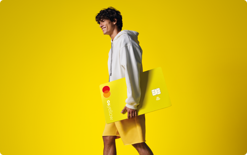 Menino sorri enquanto caminha segurando cartão C6 Yellow ampliado. Fundo e roupas seguem tom amarelo vibrante.