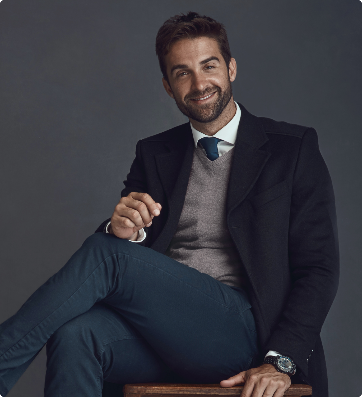 Homem de blazer, sentado em uma cadeira e de pernas cruzadas