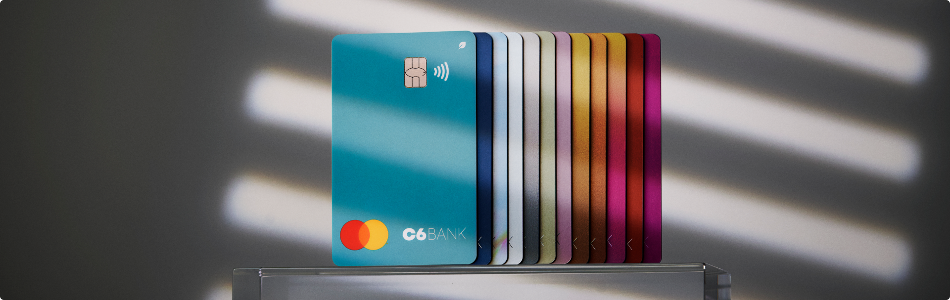 Cartões C6 Bank coloridos em leque com destaque para a cor Acqua.